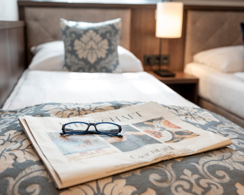 Zeitung und Brille auf dem Bett im Zimmertyp Cosy © Lorenz Masser